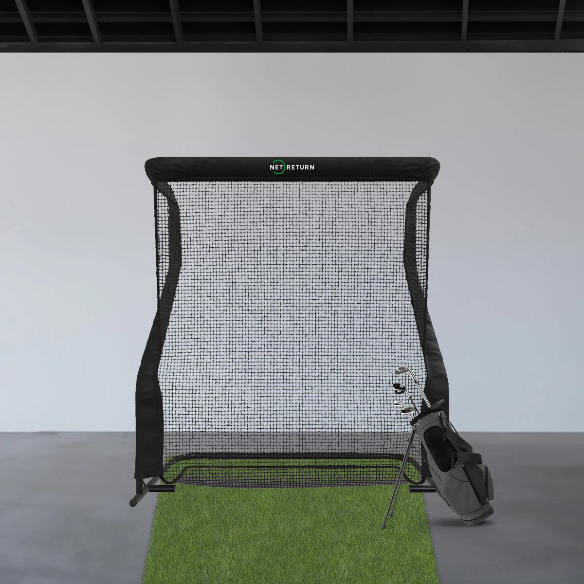 Filet de practice de golf Net Return Pro Series installé sur une surface en gazon synthétique, avec un sac de clubs de golf posé à droite. Idéal pour l'entraînement en intérieur, ce filet robuste renvoie les balles automatiquement vers le joueur.