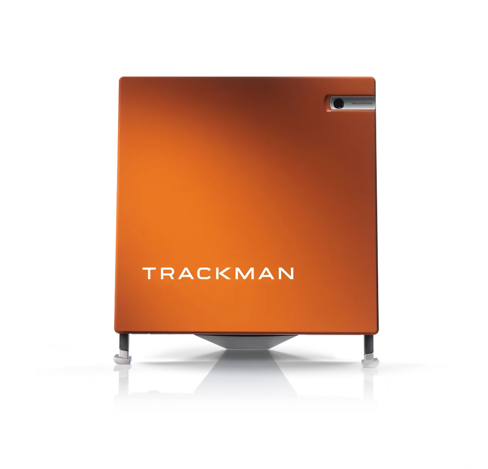 L'image présente trois vues d'un appareil TrackMan, un moniteur de lancement de golf. L'appareil est de forme carrée et compact avec une face avant orange portant l'inscription "TrackMan". Cet appareil est conçu pour analyser les performances de golf, capturant les données sur le swing et le vol de la balle.